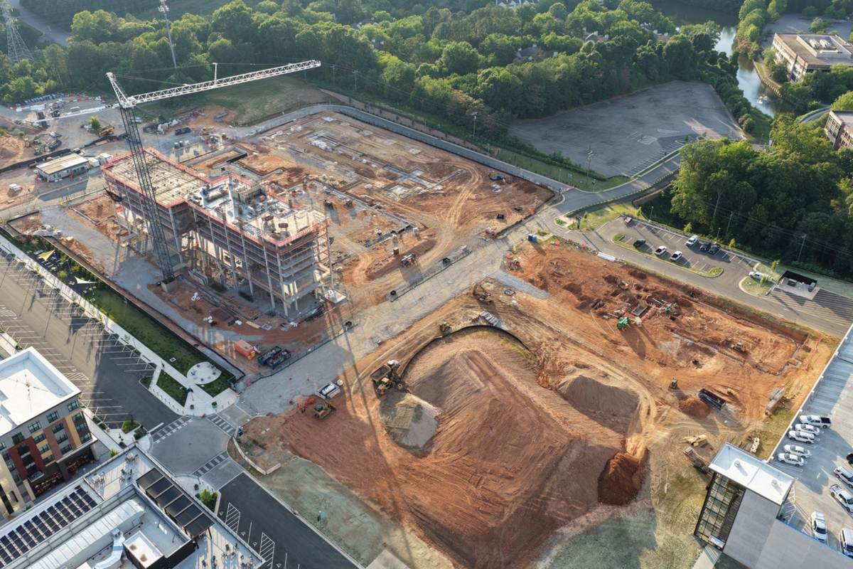 Large commercial development aerial progress photo with crane, grading, site logistics, and construction staging